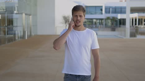 Front-view-of-focused-young-man-talking-on-smartphone.
